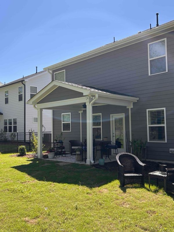 Backyard patio with furniture, next to a gray house on a sunny day.