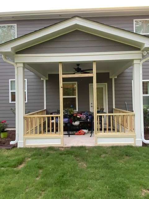A newly constructed screened porch with light wood railings, set against a gray house with white trim.