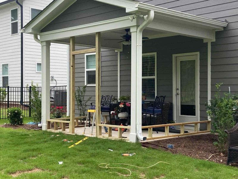 Construction of an outdoor covered patio with wooden framework on green grass, near a house.