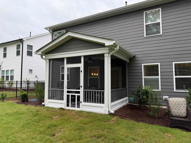 Screened porch with gray siding, white trim, and dark gray screens. Lawn and garden in foreground.