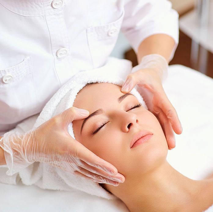 A woman is getting a facial treatment with a towel wrapped around her head.