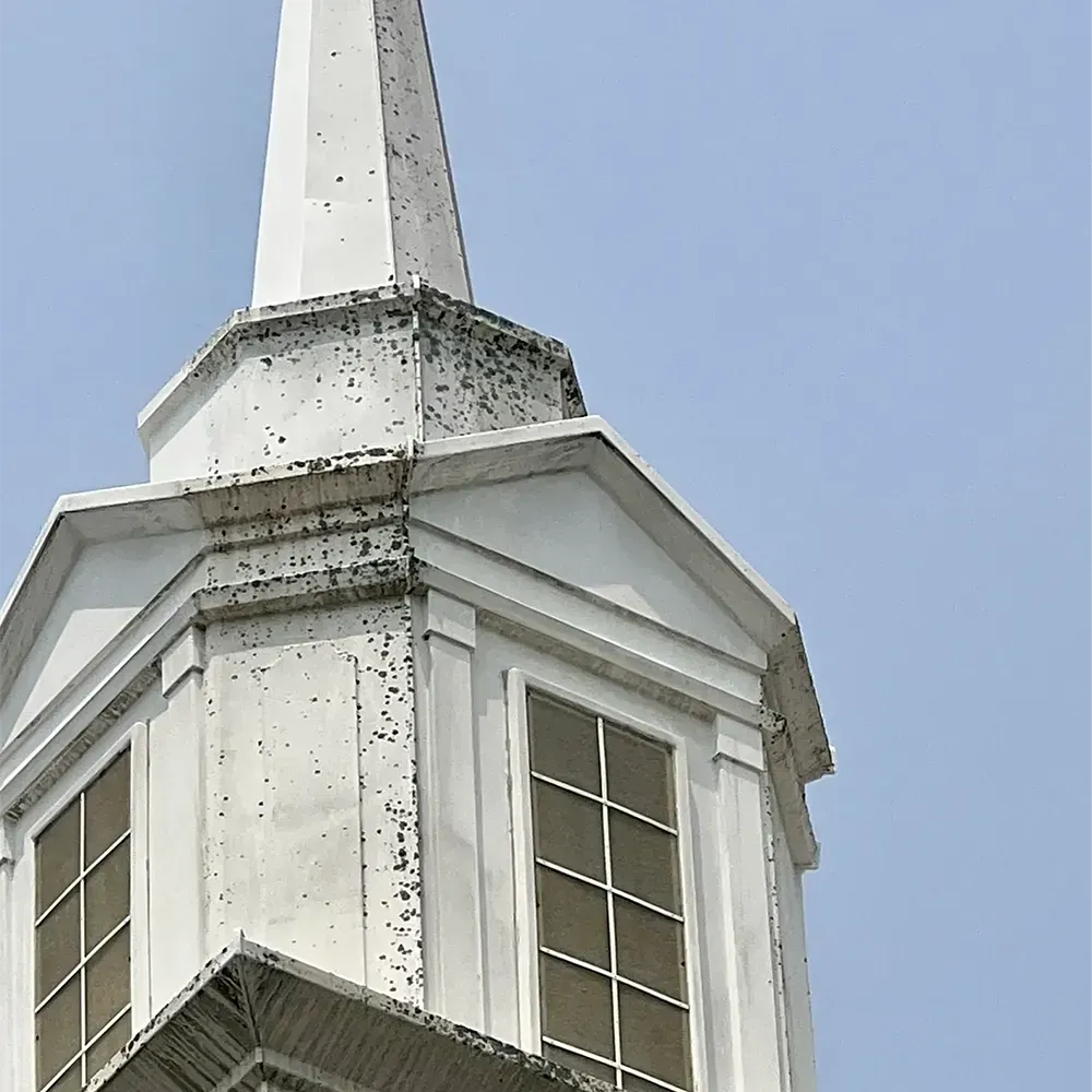 White church steeple with tall spire and windows against a blue sky
