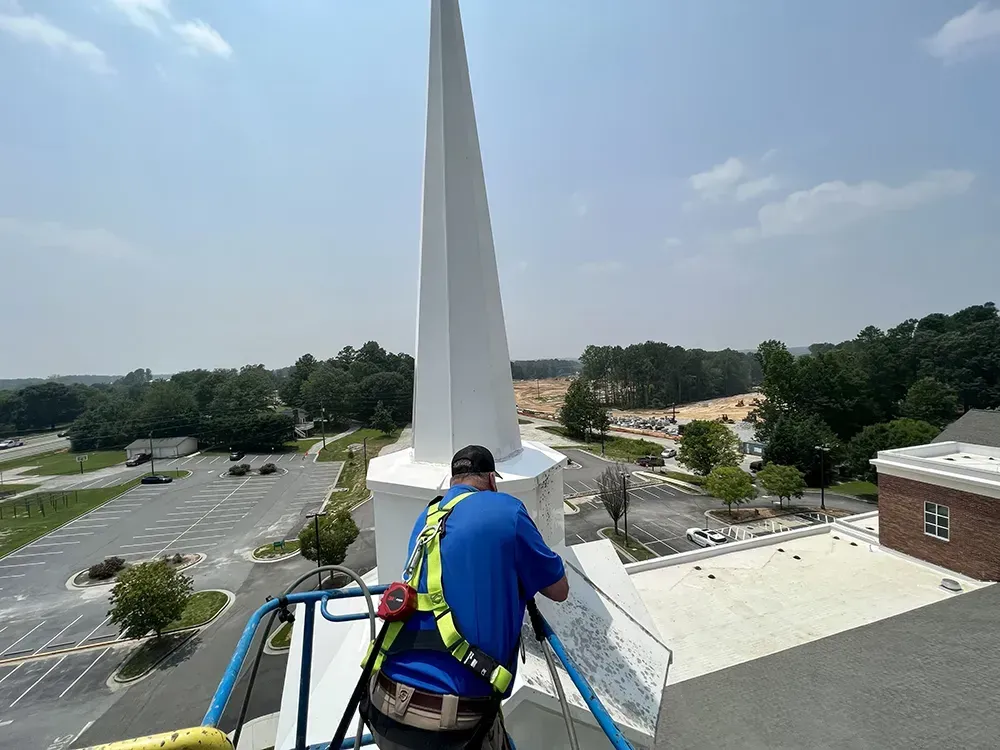 Person in blue shirt on a rooftop, overlooking a tall white monument and parking lot below