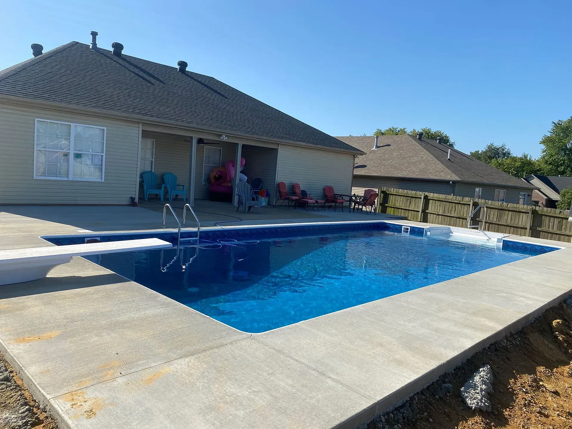 A rectangular pool with blue water and concrete borders next to a house with a dark roof.