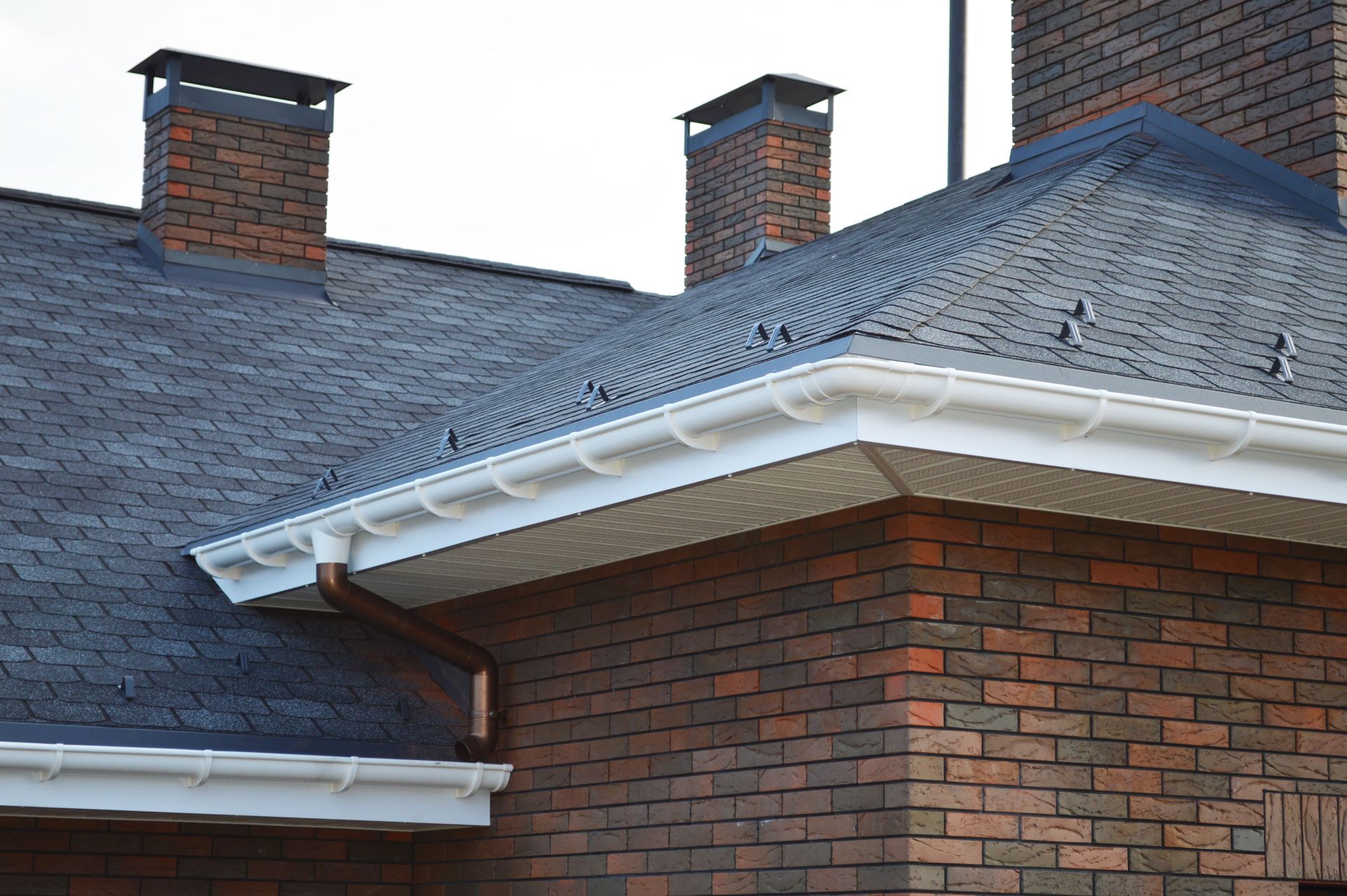Brick building with a dark shingled roof, white gutters, and two brick chimneys.