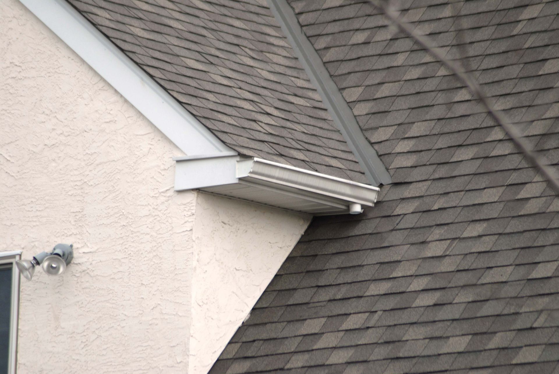 A house with a light-colored stucco wall and a dark, shingled roof.