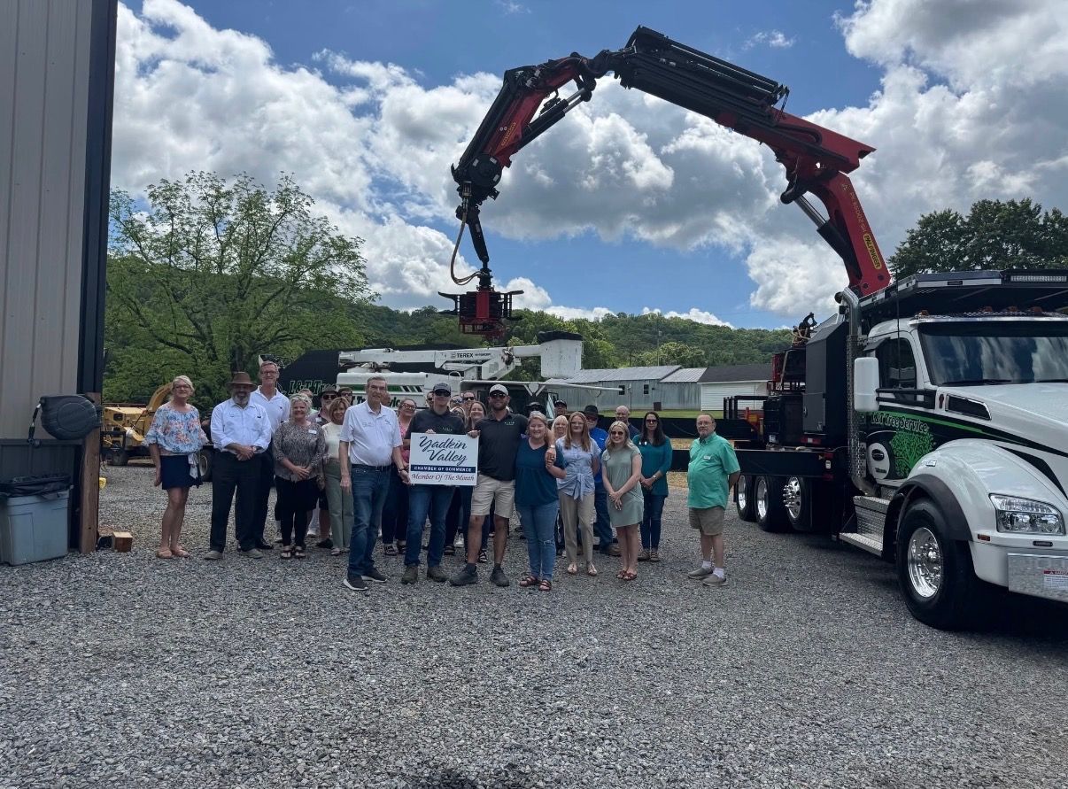 Group standing beside a white crane truck with a raised black-red boom in a gravel lot.