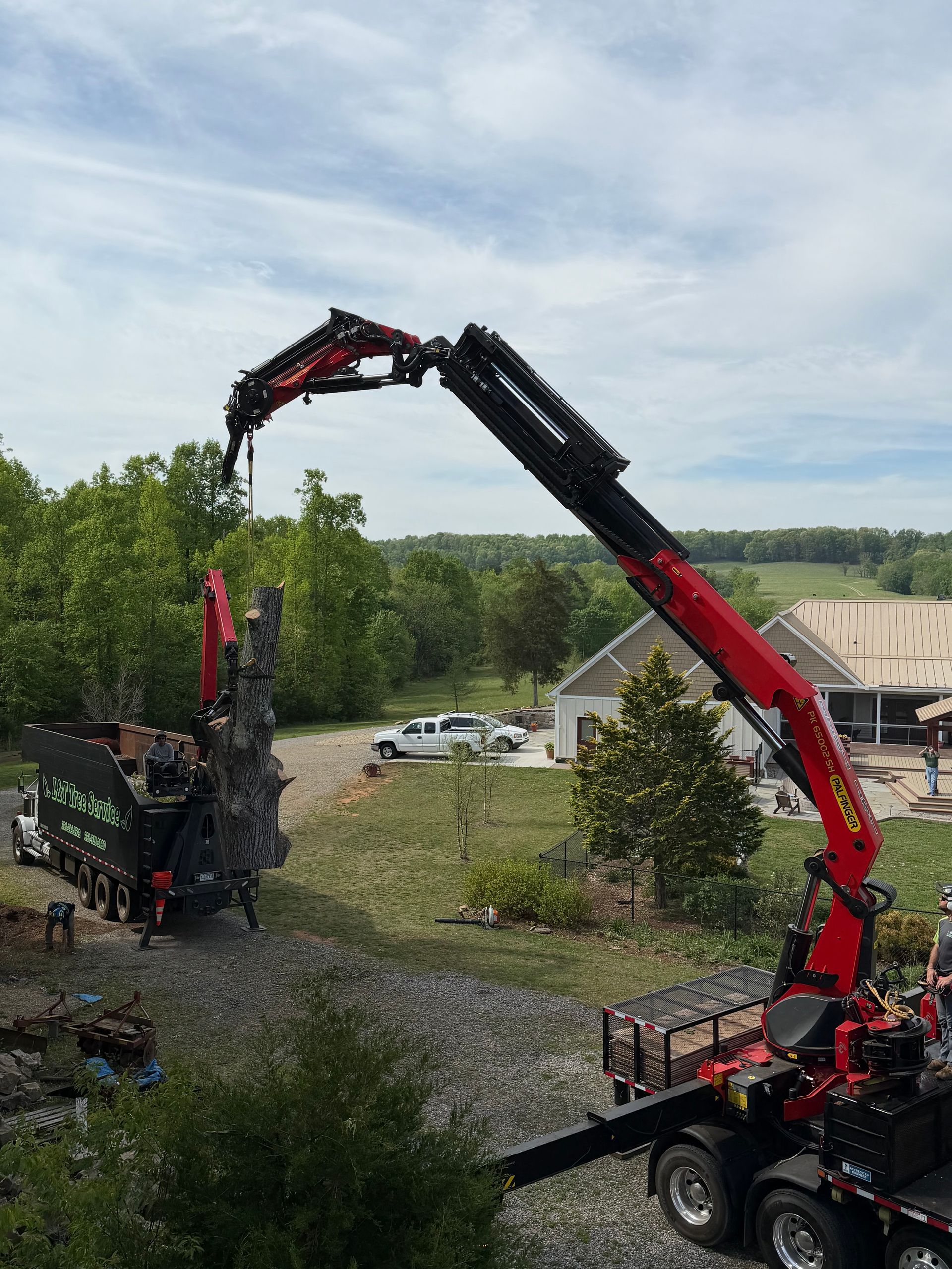 Red crane lifts a load of black debris beside a gravel road in a green rural field.