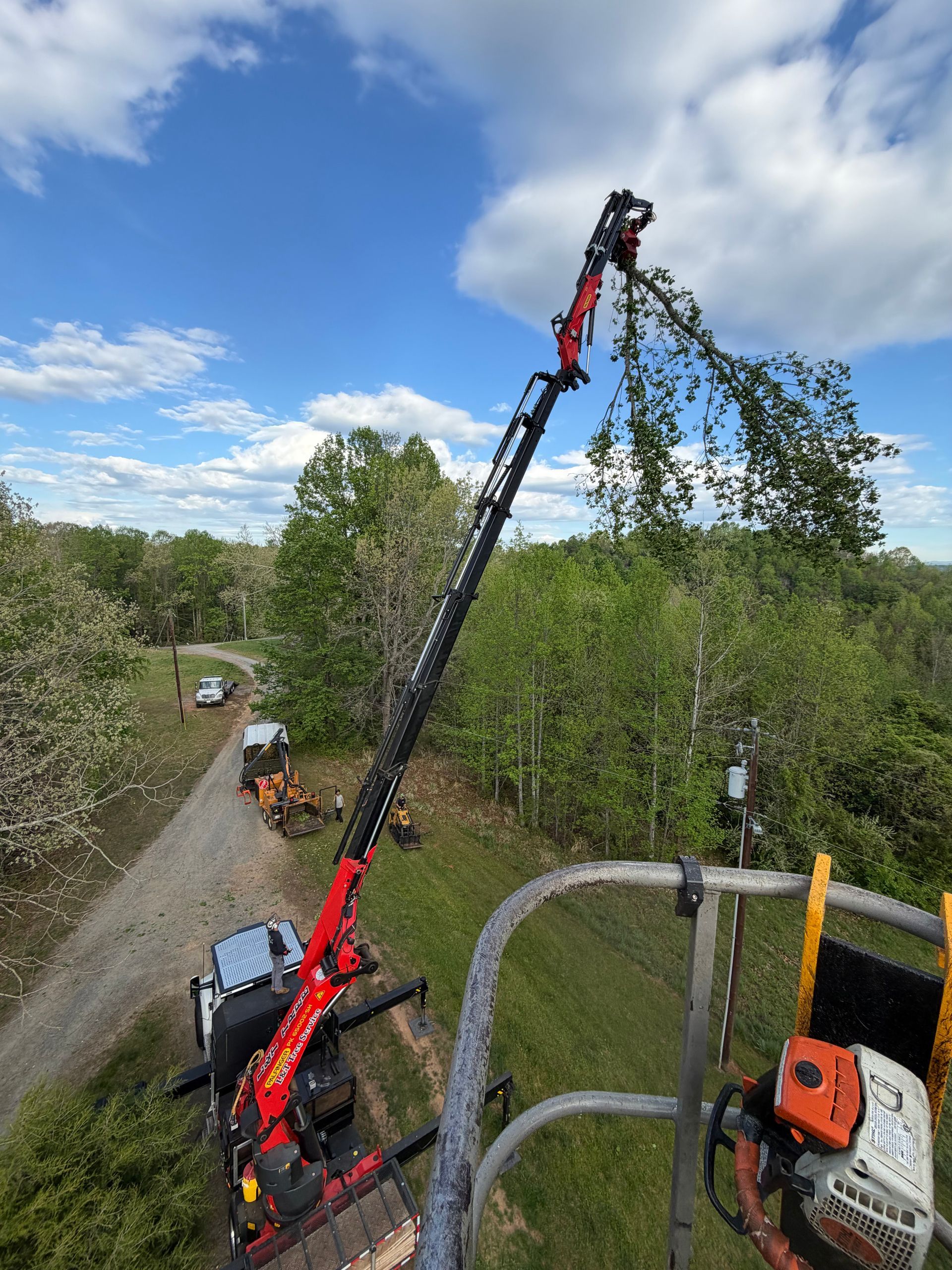 Red forestry crane lifting branches over a dirt road under a blue, cloudy sky