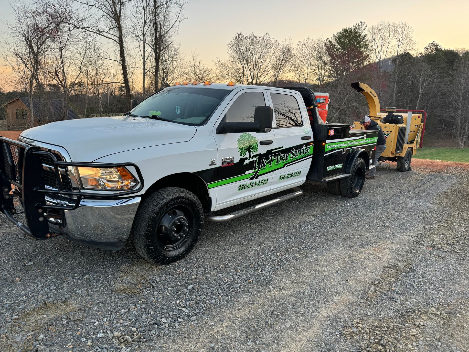 White tree service truck with a wood chipper on a trailer, parked on gravel.