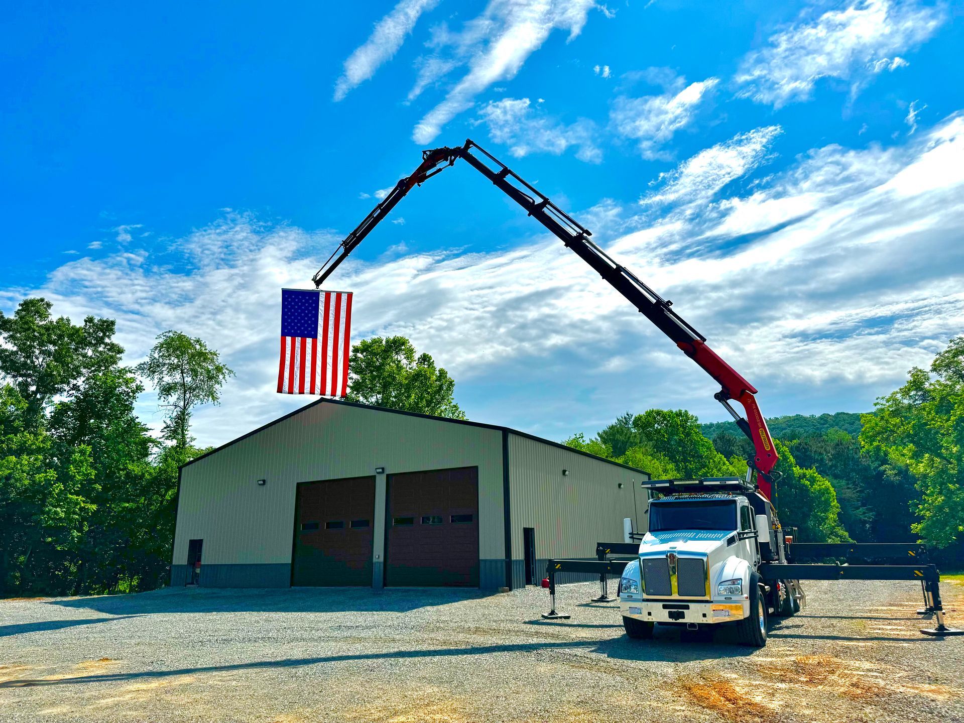 Truck crane holding American flag in front of a building with blue sky background.