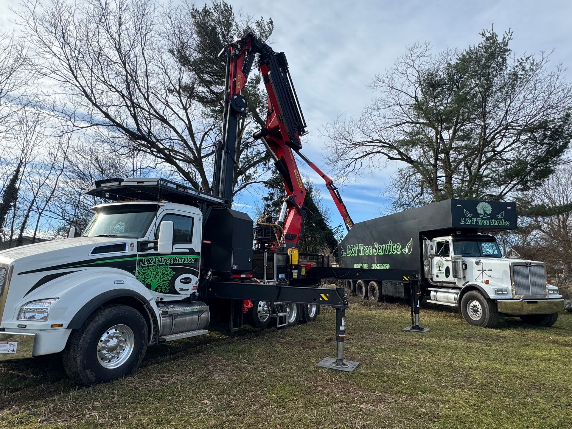 White and green tree service trucks with raised crane in a grassy area.