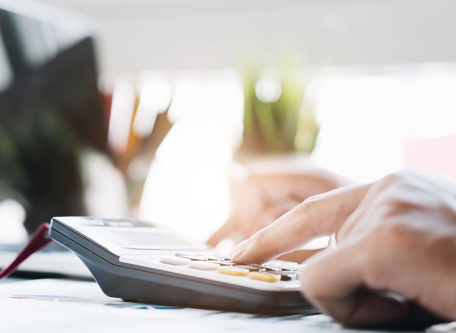 Person using a calculator with fingers on the buttons, possibly at a desk.