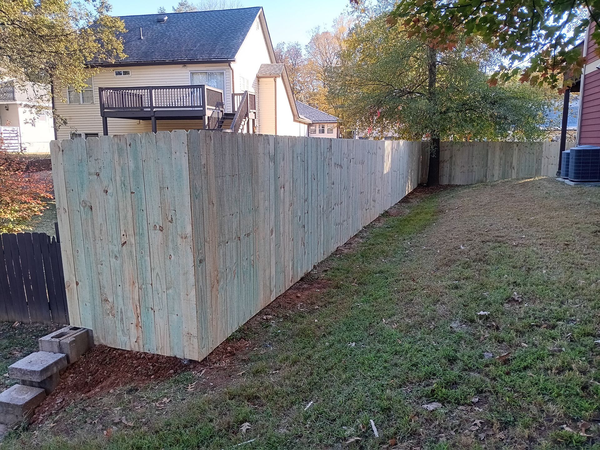 Wooden fence in a yard next to grass and a building. Autumnal colors.