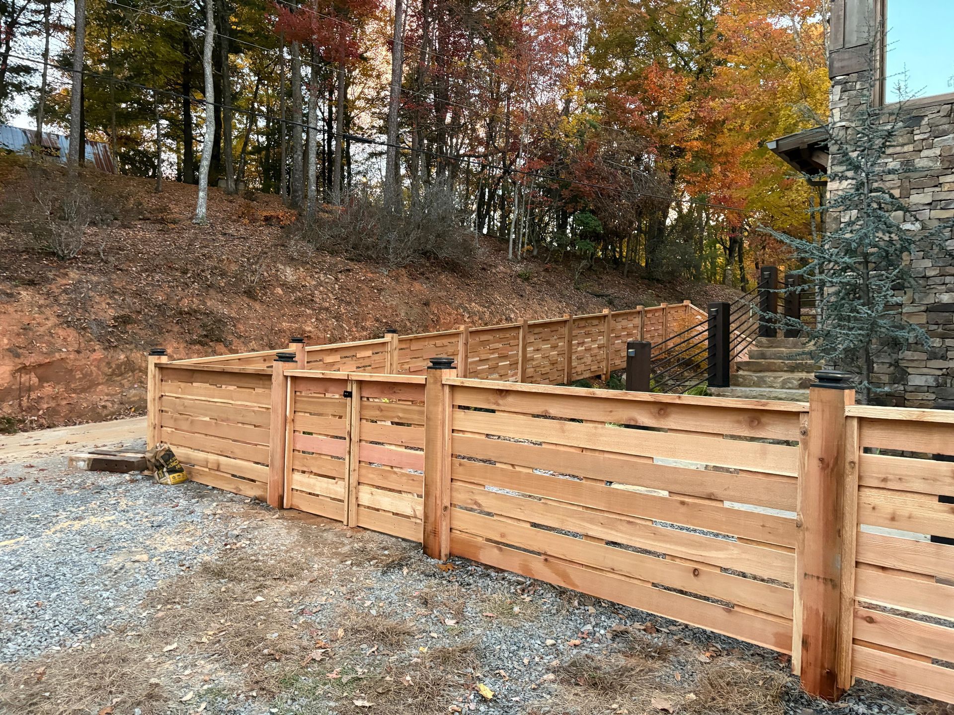 Wooden fence with gate in front of a hillside with colorful autumn foliage.