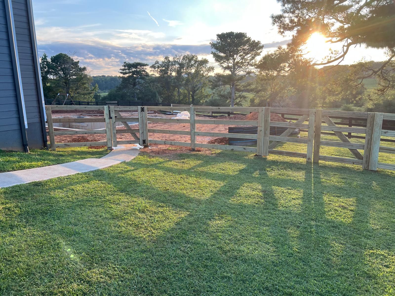 Wooden fence with gate, leading to a yard, with sunlight.