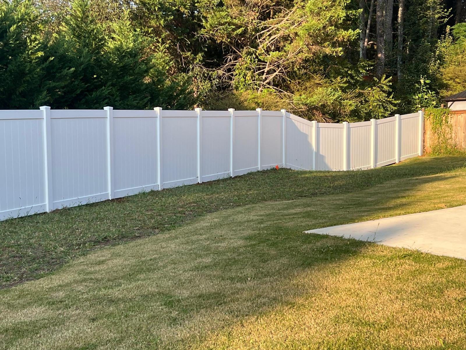 White vinyl fence surrounds a grassy backyard, trees in the background, sunny day.