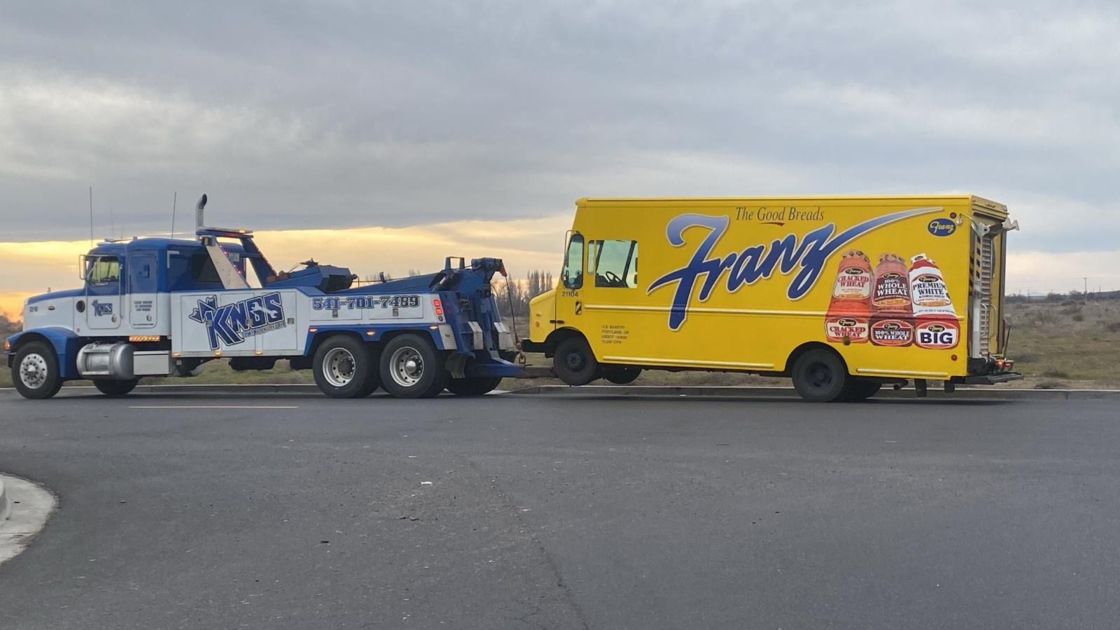 A blue and white tow truck is towing a yellow food truck.