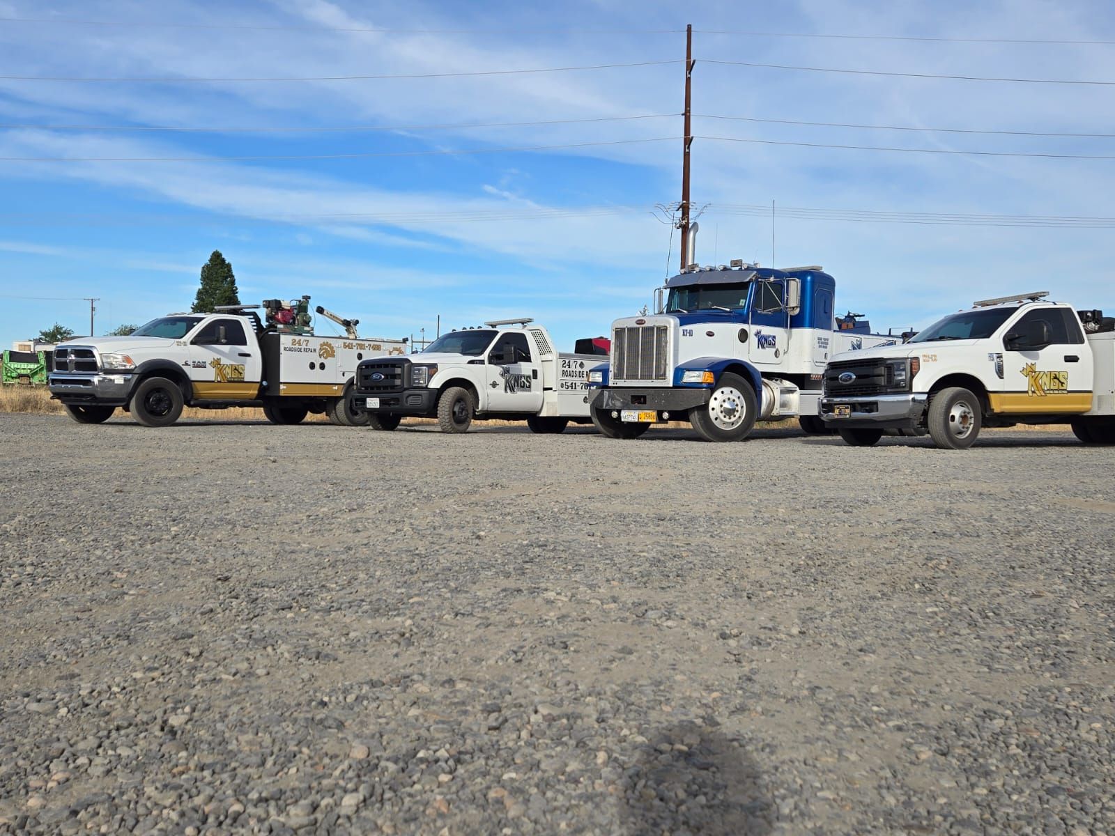 A row of tow trucks are parked in a gravel lot.