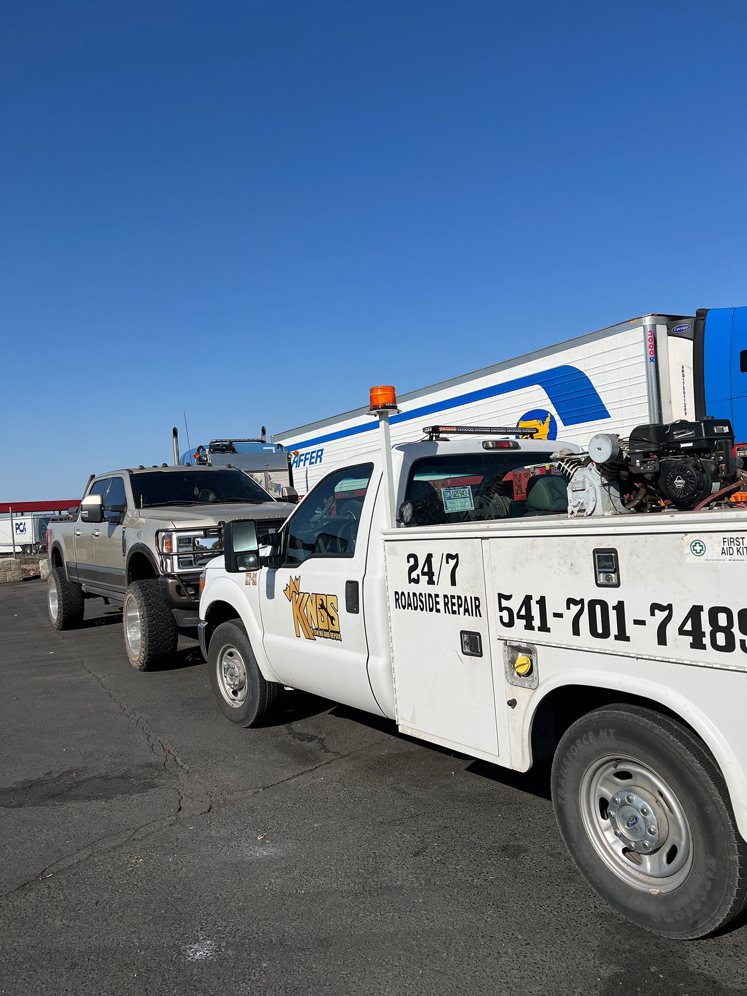 A white tow truck is parked next to a white truck.