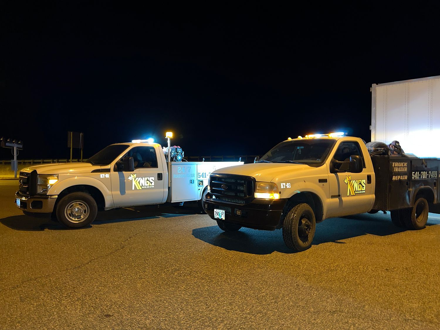 Two tow trucks are parked next to each other in a parking lot at night.