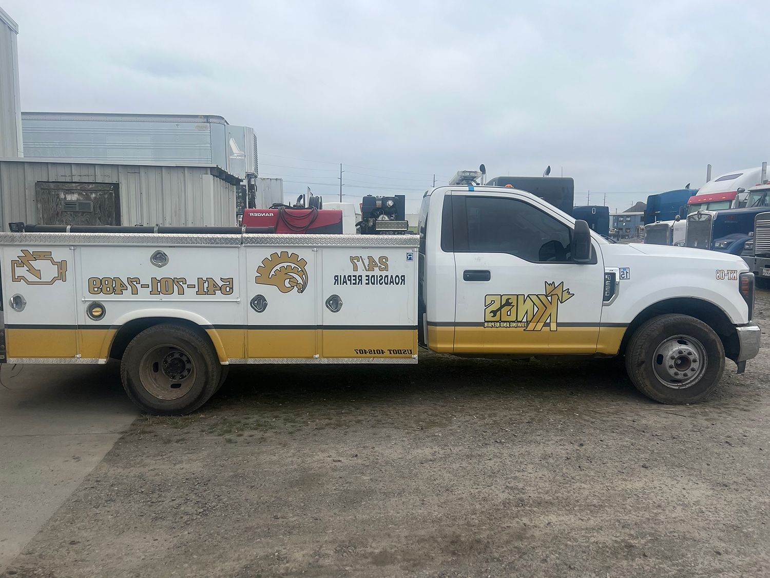 A white and yellow tow truck is parked in a gravel lot.