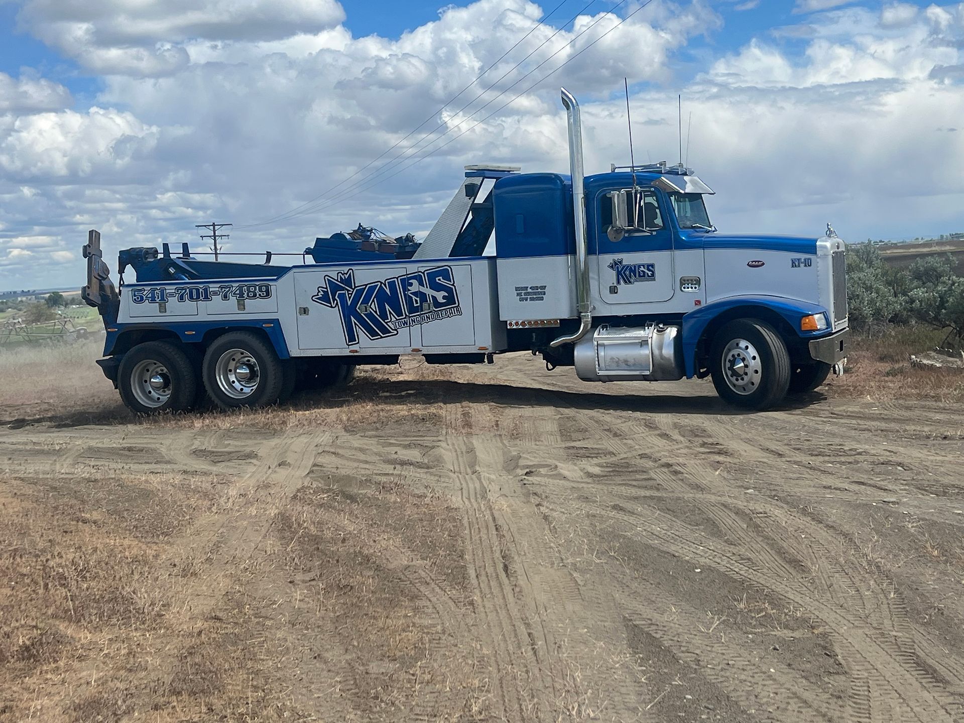 A blue and white tow truck is driving down a dirt road.