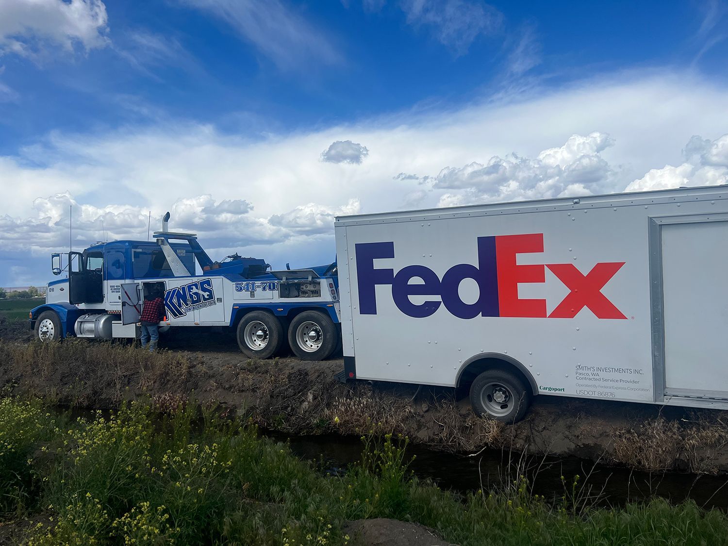 A fedex truck is towing a trailer in a field.