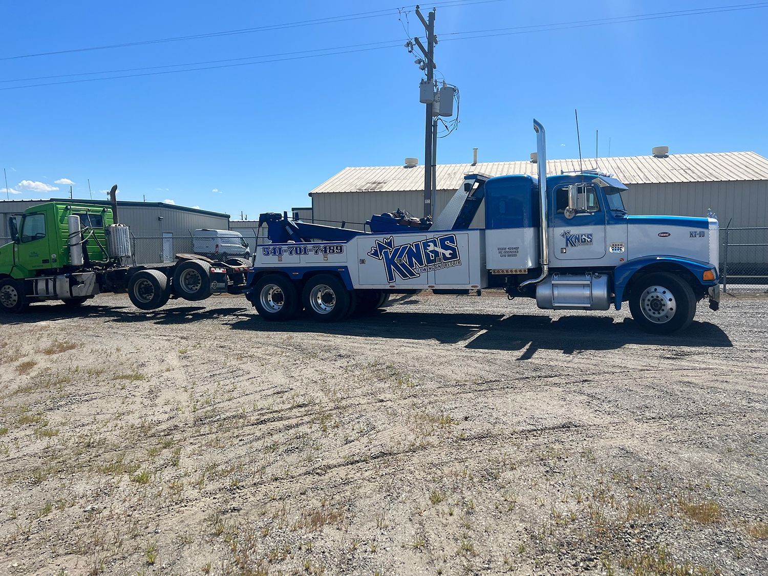 A blue and white tow truck is parked next to a green truck.