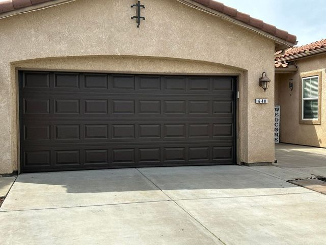 Tan house with a dark brown double garage door and concrete driveway under a tiled roof.