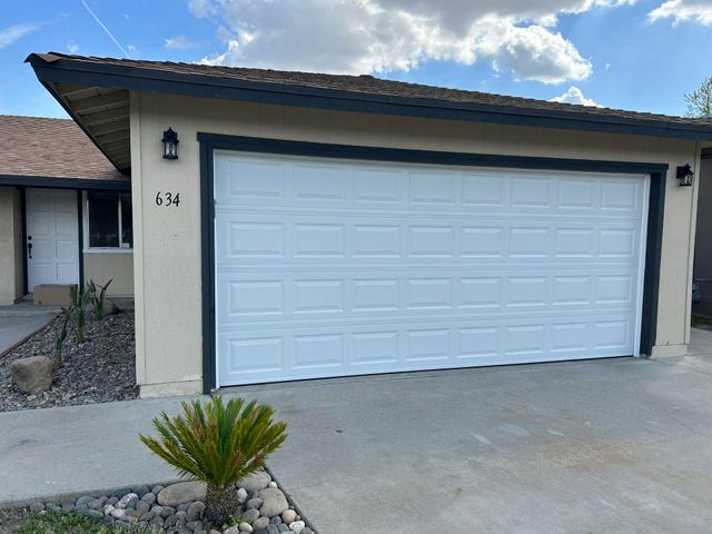 Suburban home exterior with a white garage door, beige stucco walls, and a small plant in the driveway