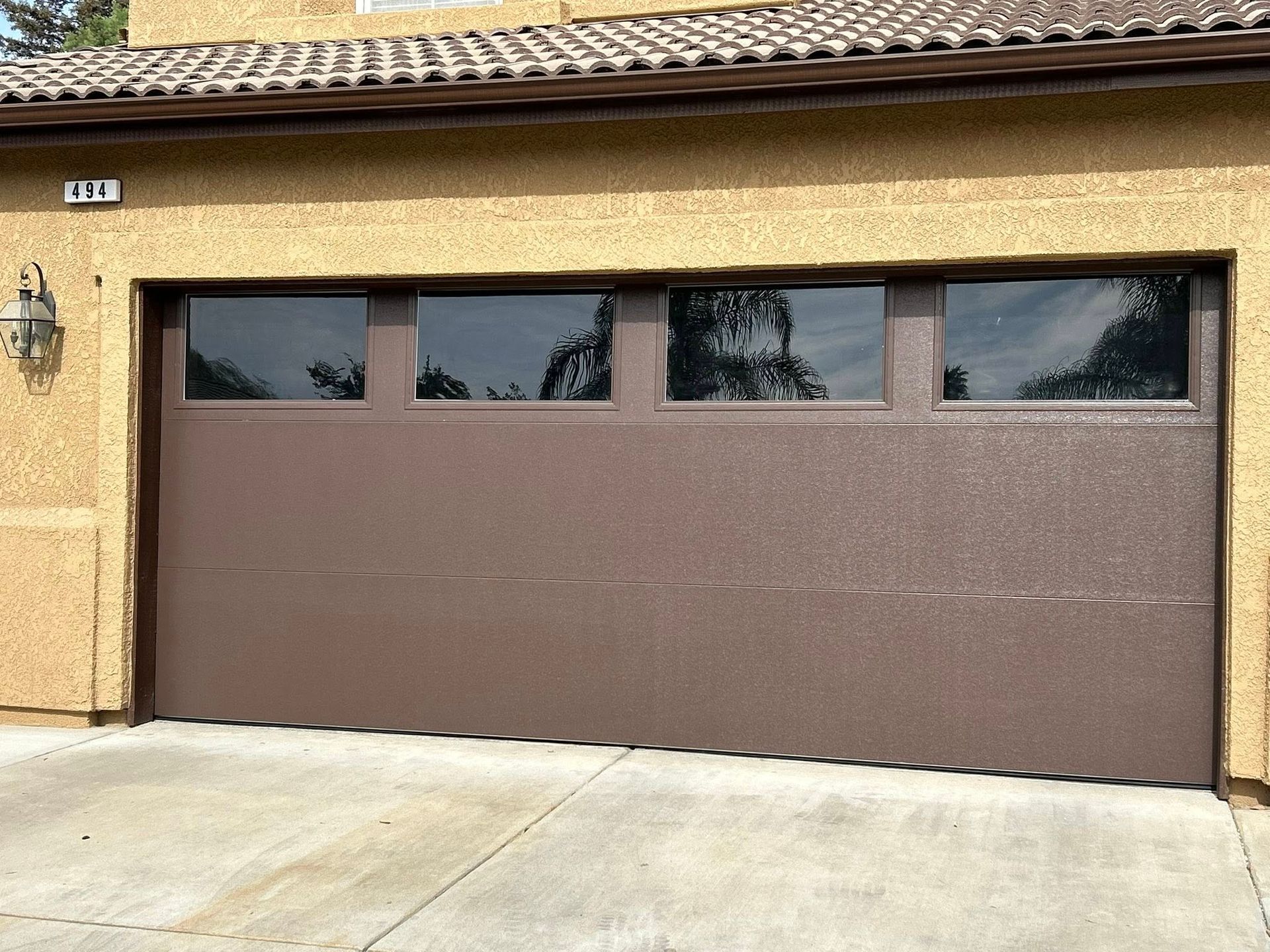 Brown two-car garage door on a beige stucco house with narrow windows across the top.