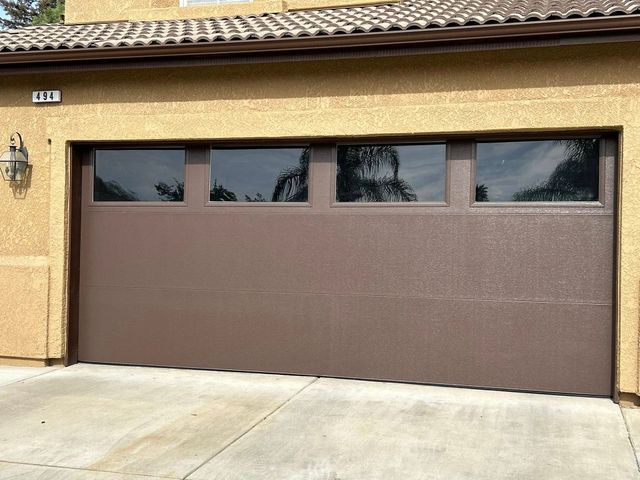 Brown two-car garage door on a beige stucco house with narrow windows across the top.