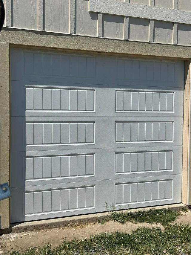 Gray garage door with six white window panels on a beige exterior wall.