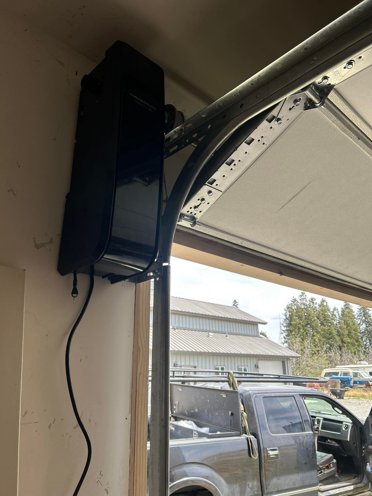Black garage door opener mounted on a garage ceiling beside an open door with a vehicle outside