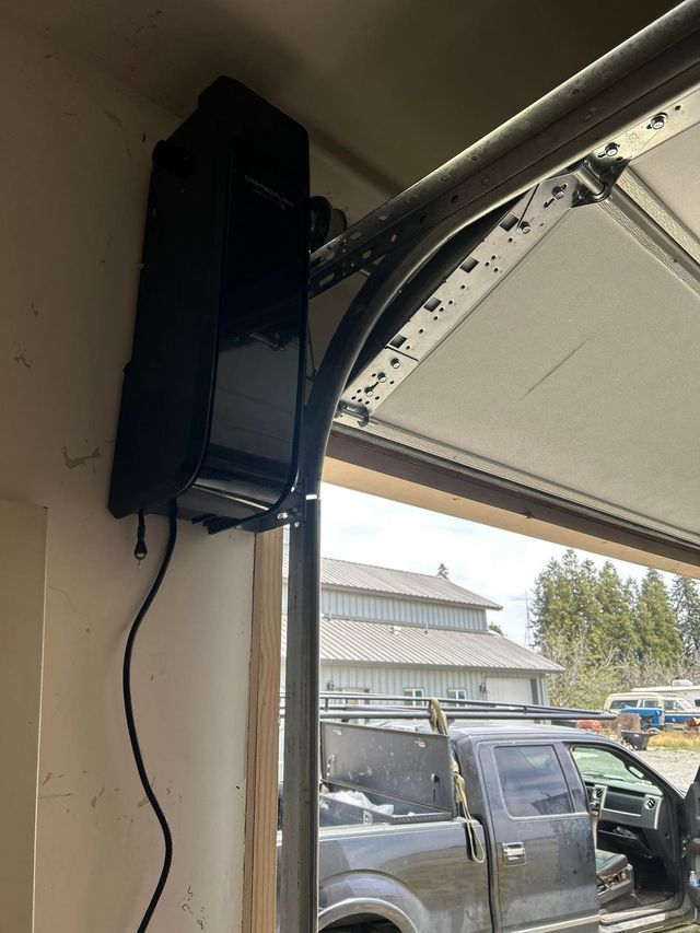 Black garage door opener mounted on a garage ceiling beside an open door with a vehicle outside