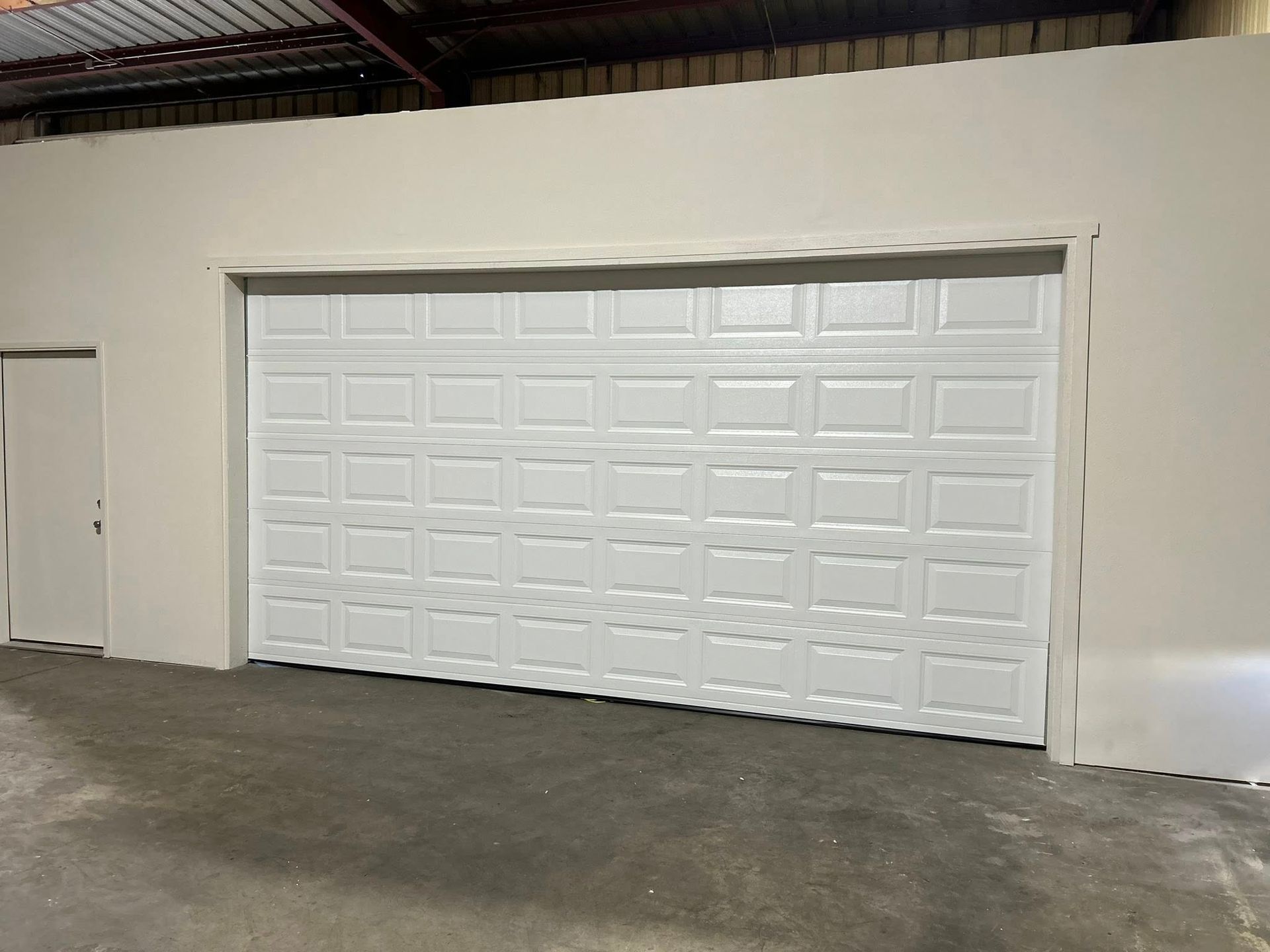 White garage door set in a beige industrial building interior with a concrete floor.