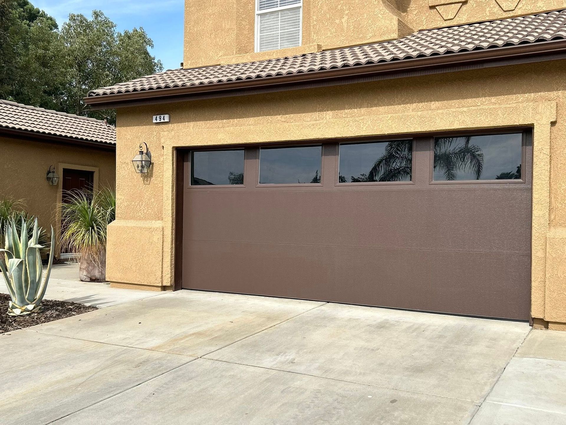 Tan stucco house with a brown garage door and a driveway in front