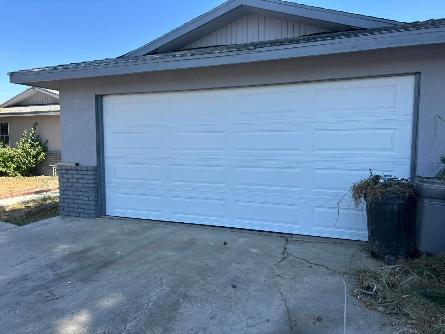 White two-car garage with a concrete driveway and a black trash bin beside it.