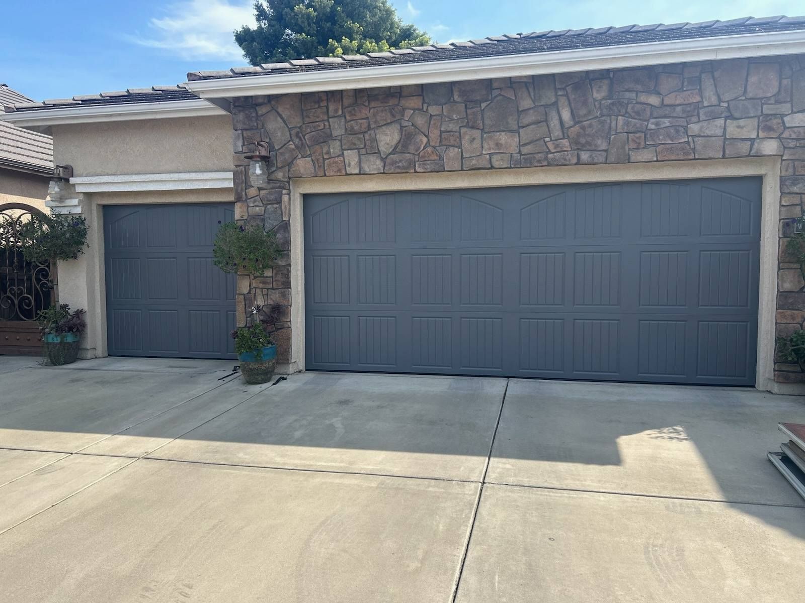 Two-car garage with gray doors and stone facade on a sunny suburban house