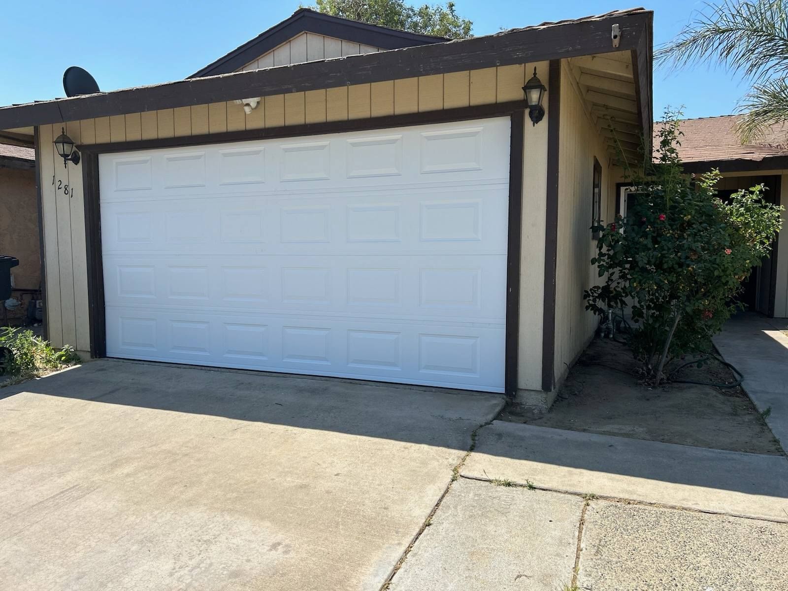 Single-car garage with white door, tan trim, and driveway in a residential area
