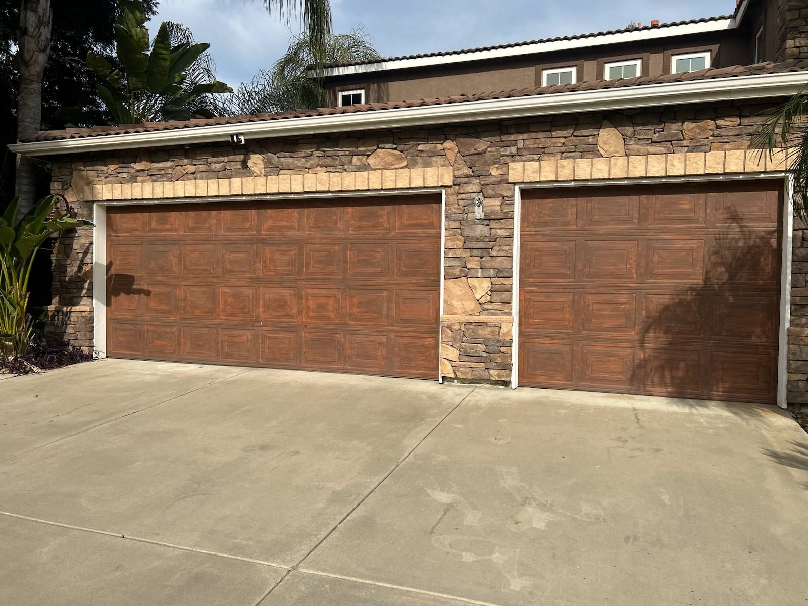 Two brown garage doors on a stone house with a concrete driveway