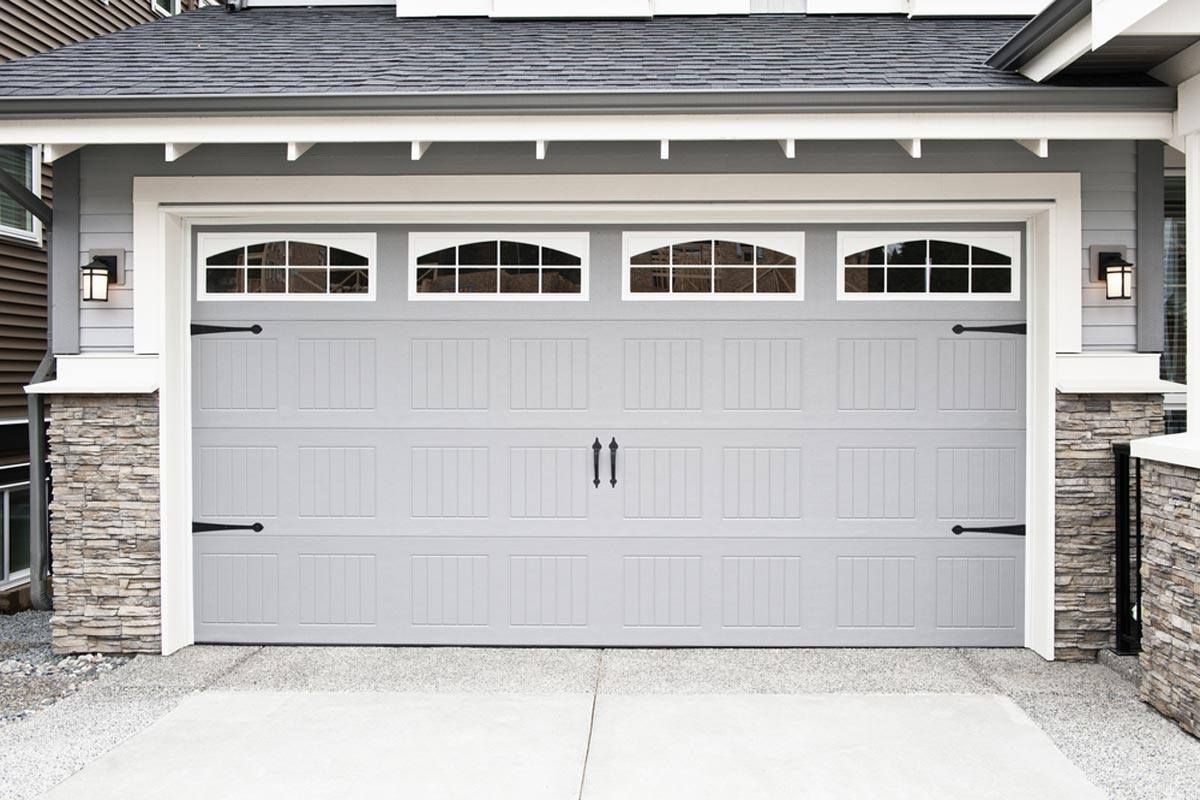 White double garage door with small windows beneath a house overhang.