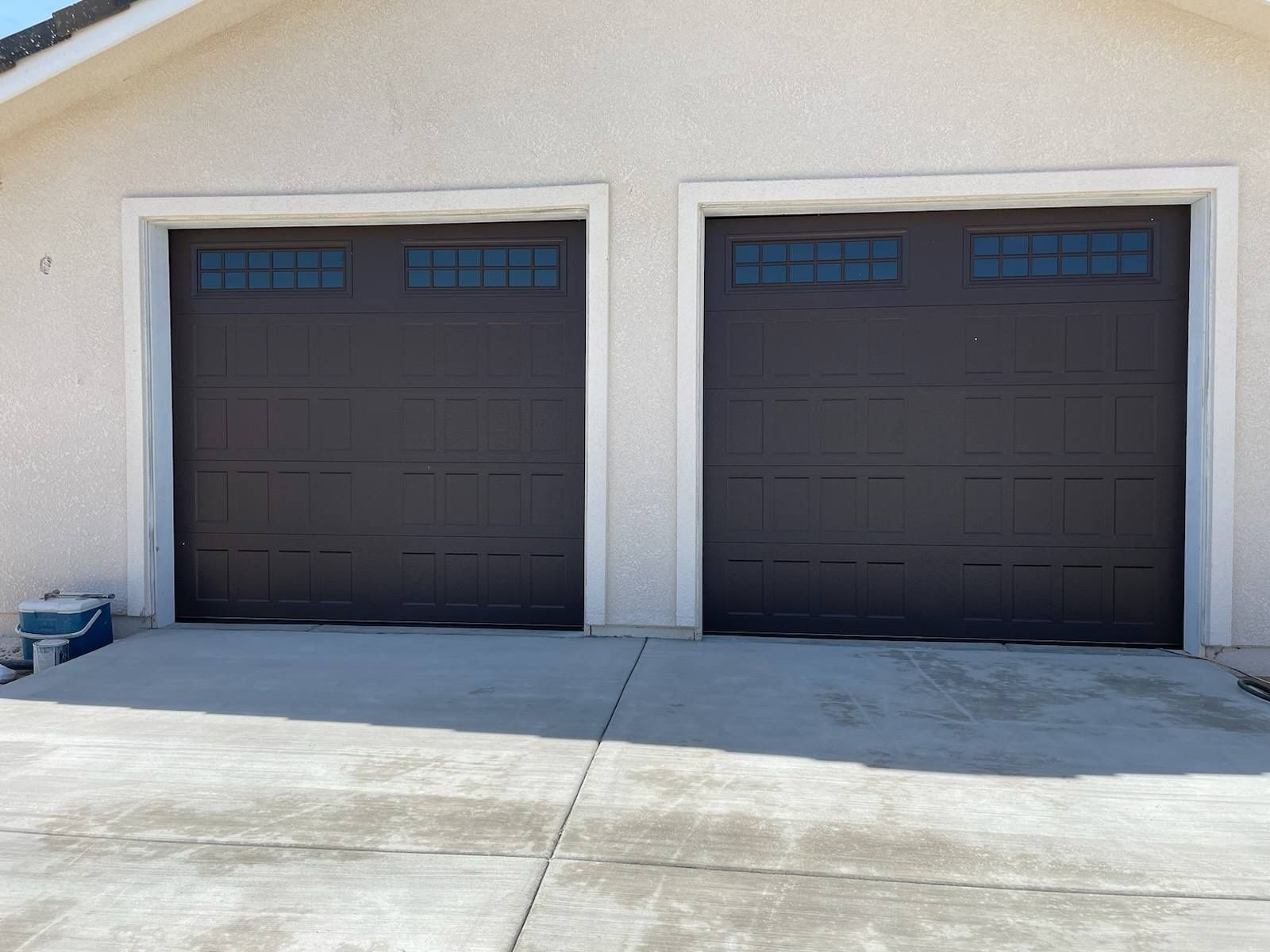 Two dark garage doors in a white stucco exterior wall above a concrete driveway