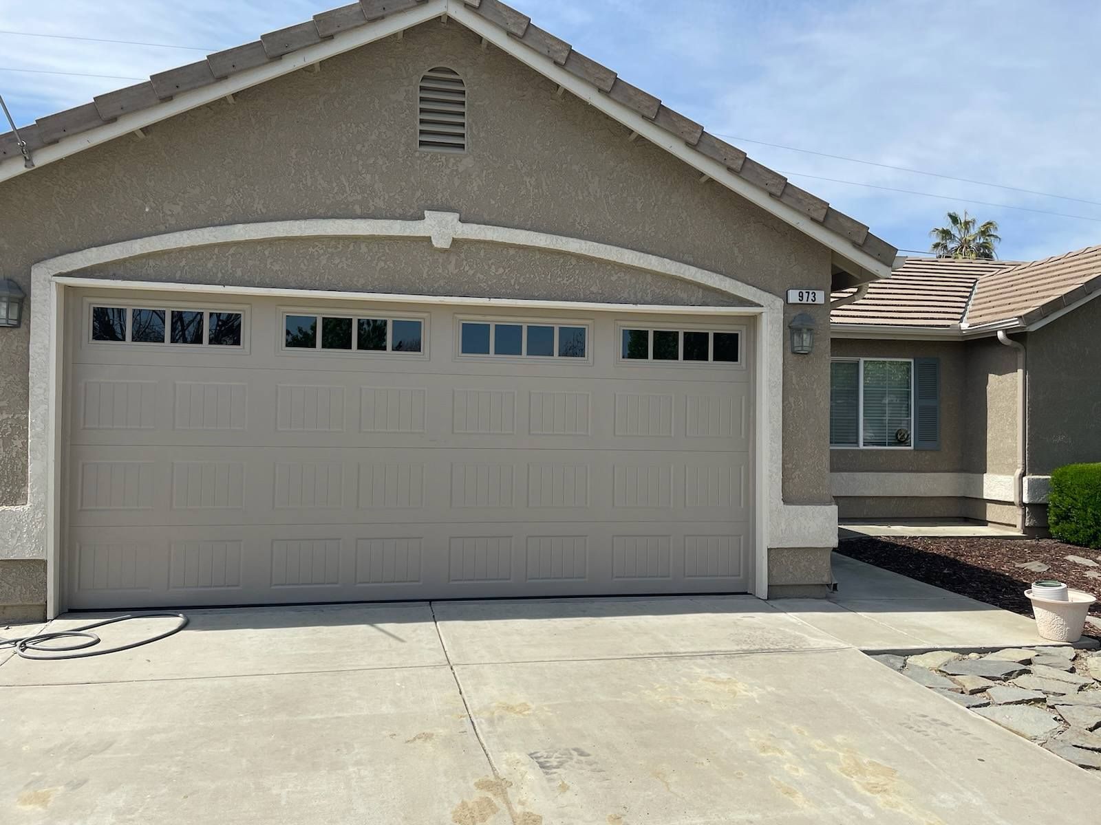Suburban house exterior with a beige two-car garage and concrete driveway under a blue sky