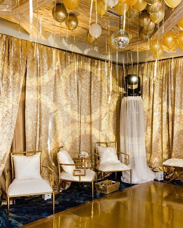 A room with gold curtains and chairs and balloons hanging from the ceiling.