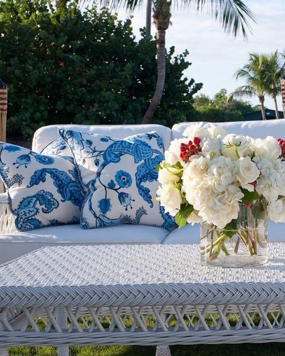 A white couch with blue and white pillows and a vase of flowers