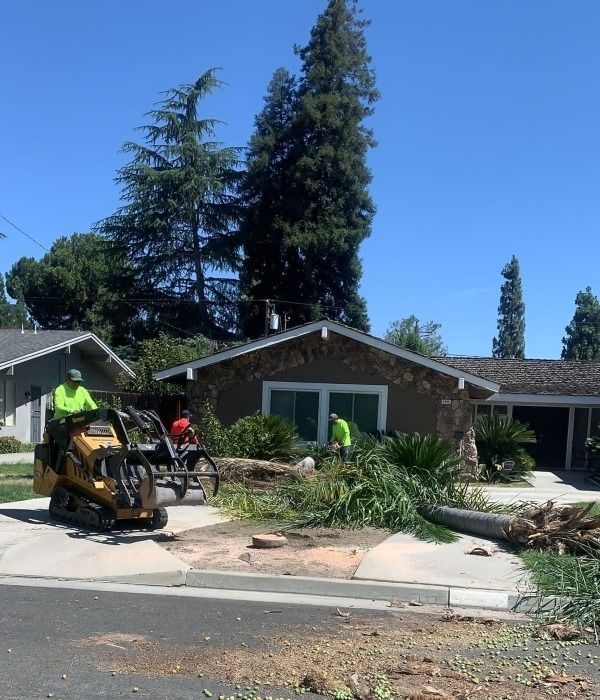 Workers clearing debris in front of a suburban house after storm damage