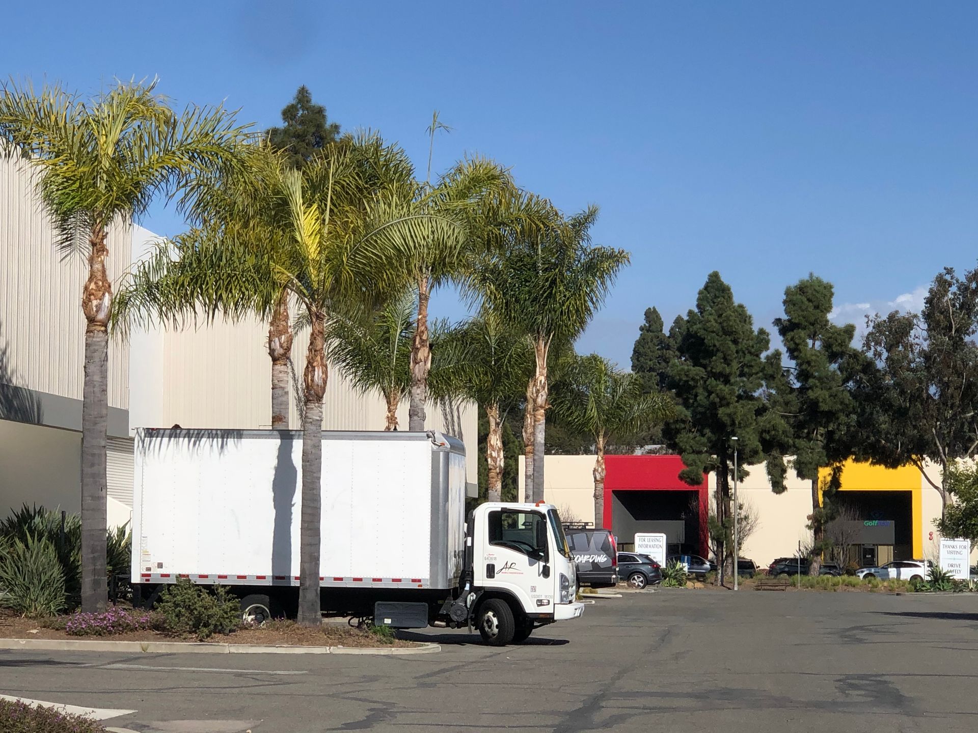 White box truck parked outside a building with palm trees under a clear blue sky