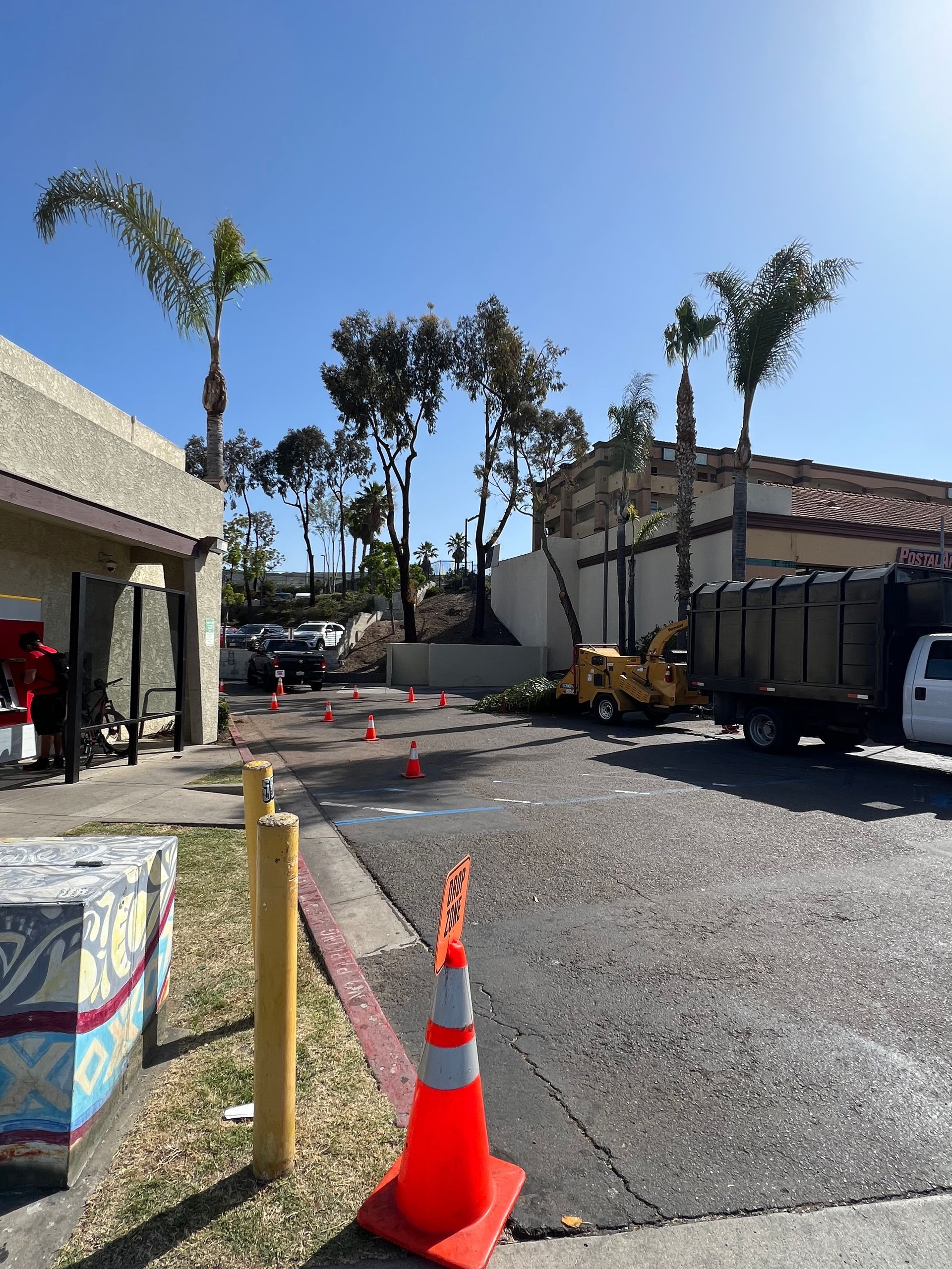 Construction zone with orange cones and gravel path beside buildings under a clear blue sky